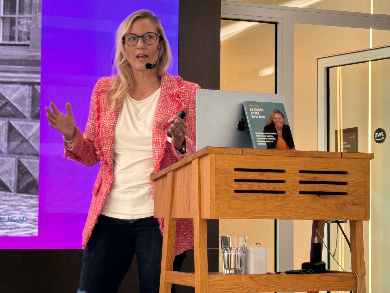 Verena Laumayer speaking at a lectern in front of a purple screen at the AWS Munich office